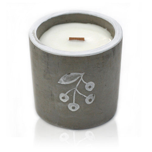 A concrete candle with a wooden wick and a print of juniper berries on the side, containing a white candle.