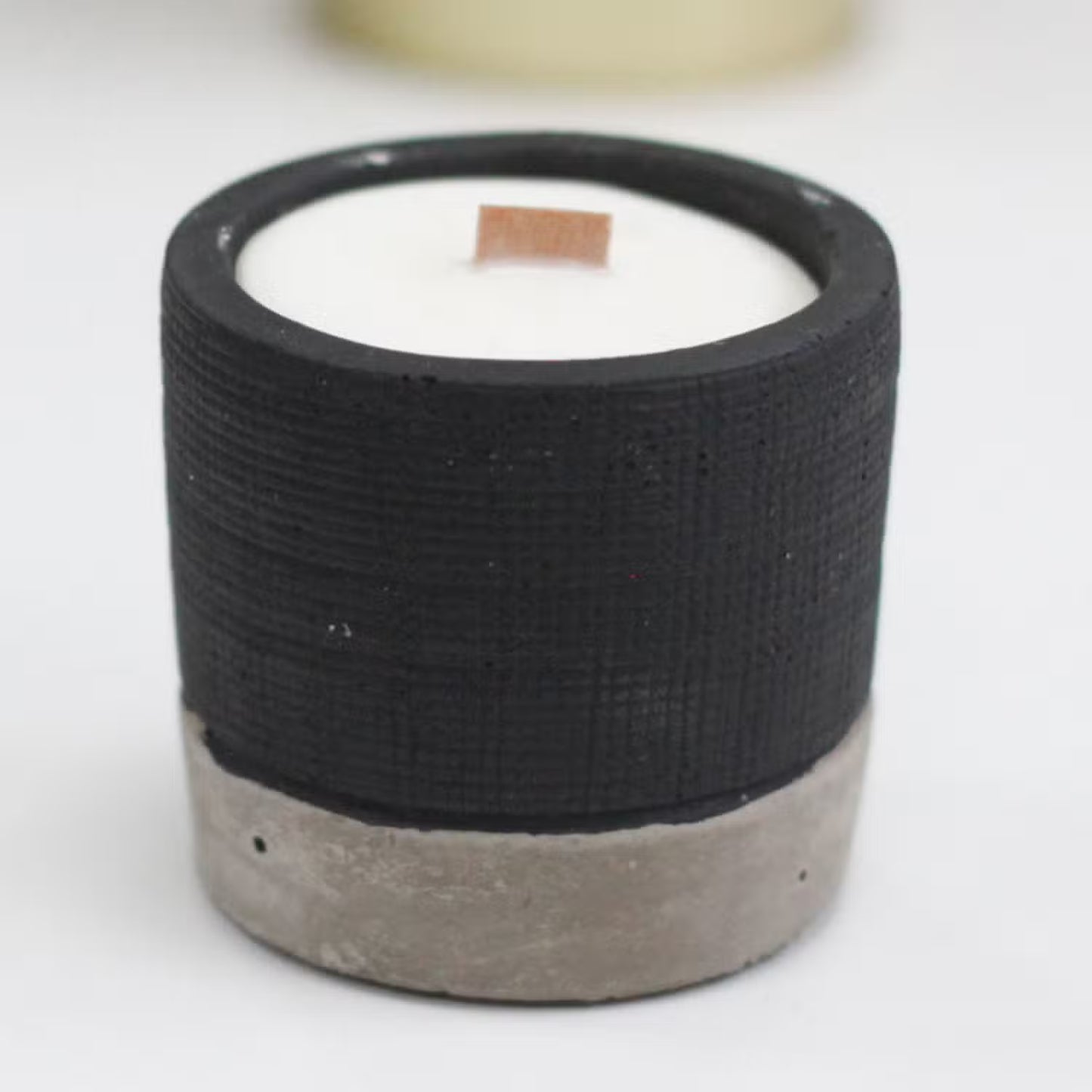 Candle in a black textured container with a concrete base on a white background
