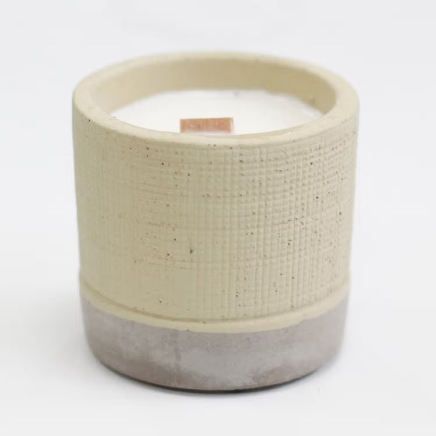 Ceramic candle with textured beige top and concrete base on a white background